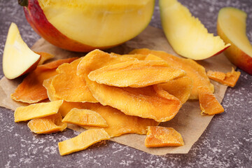 Baking paper with slices of dried mango on dark table