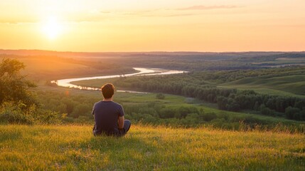 Serene sunset view, man meditates atop grassy hill overlooking winding river valley