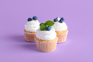Tasty cupcakes with blueberries on lilac background