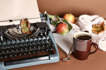 Vintage typewriter, cup of coffee, notebook and autumn leaf on brown background