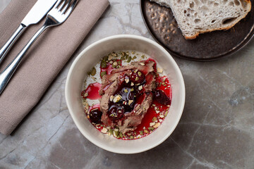 Savor the rich flavors of contemporary European cuisine with a beautifully arranged meat dish topped with a vibrant fruit sauce, set on a rustic table in an inviting restaurant