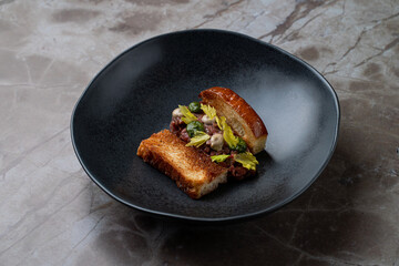 A beautifully crafted sandwich sits gracefully on an elegant black plate, featuring a rich filling of savory ingredients, garnished with fresh greens