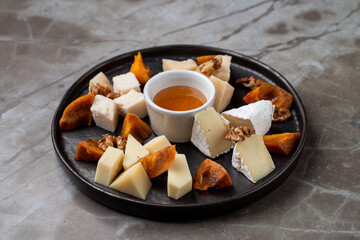A delectable assortment of artisanal cheeses arranged beautifully on a black plate, enhanced with honey and walnuts, inviting guests to savor fine European flavors at a cozy restaurant