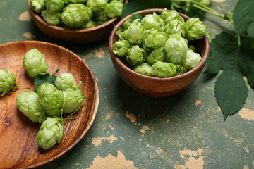 Wooden bowls and plate with fresh green hops on color background