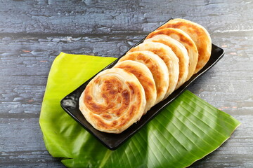 Golden brown porotta served on a white plate with a wooden background.