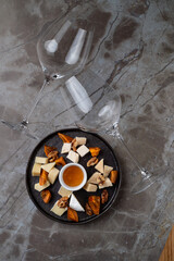 An exquisite arrangement of gourmet delicacies features a selection of cheeses, dried fruits, and a honey dip, complemented by elegant wine glasses. Perfect for a fine dining experience