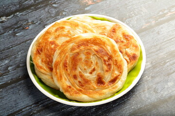Golden , flaky porottas served  on a rustic wooden table.