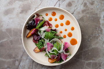 A beautifully presented salad showcases an array of fresh greens, colorful vegetables, and elegant sauces, perfect for an upscale European restaurant setting