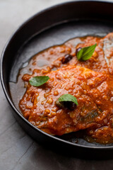 A beautifully plated dish of fish smothered in a savory tomato sauce, garnished with fresh herbs, awaits guests at a sophisticated European restaurant, creating a delightful dining experience