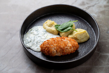 A beautifully arranged plate features a golden-brown croquette alongside smooth mashed potatoes and a delicate spinach garnish