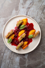 A beautifully arranged plate features succulent meat paired with fresh fruit and a rich berry sauce. This culinary masterpiece highlights exquisite techniques