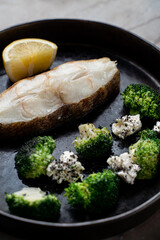 A beautifully arranged plate presents a succulent piece of fish accompanied by vibrant green broccoli florets. A slice of lemon adds a refreshing touch to this European-inspired meal