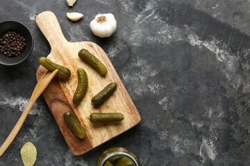 Wooden board with tasty pickled cucumbers and different spices on black background