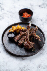 Plates of succulent lamb chops accompanied by crispy roasted potatoes and a delightful dipping sauce create an inviting atmosphere at a European restaurant