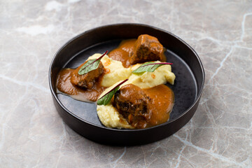 Tender meatballs bathed in a savory sauce rest atop a bed of smooth mashed potatoes, garnished with delicate leaves. This delightful dish embodies European culinary artistry