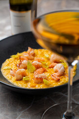 A beautifully plated seafood risotto showcases plump shrimp atop a golden creamy base, set in a sophisticated restaurant ambiance with a glass of wine nearby