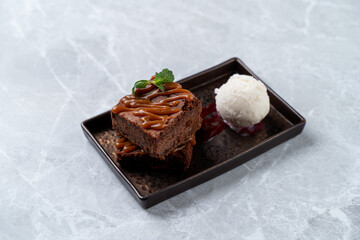 Indulging in a delicious dessert at a European cuisine restaurant, a moist chocolate cake drizzled with caramel sits next to a scoop of creamy vanilla ice cream, garnished with a mint leaf