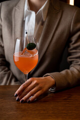 A well-dressed individual holds a vibrant cocktail garnished with a green olive in a sophisticated restaurant setting, promoting an atmosphere of relaxation and culinary delight