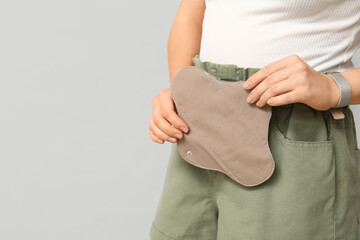 Young woman with reusable menstrual pad on light background, closeup