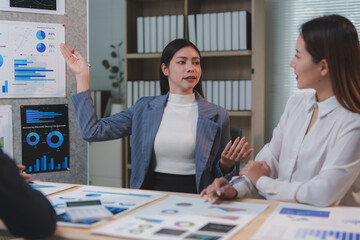 Two businesswomen are discussing company performance charts and analyzing statistics during a productive office meeting, collaborating on important business decisions