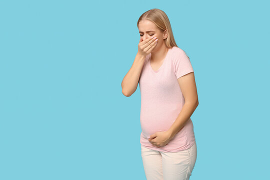 Beautiful young pregnant woman suffering from toxicosis on blue background