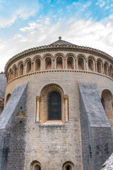 Ancient Romanesque church with arched windows and stone walls, featuring a stained-glass window, buttresses, and a blue sky