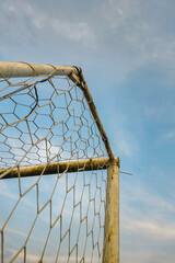 Football goal on a beautiful rural field in the morning. Detail of the top end of a slightly rusty but still usable soccer goal against a blue sky background