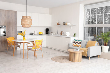 Interior of spacious stylish kitchen studio with table, armchairs, mimosa flowers, houseplant, counters and sofa