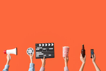 Many hands with bucket of popcorn, movie clapper and beer on orange background