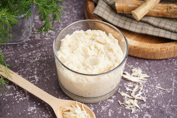 Horseradish sauce in bowl and spoon with ground horseradish on grey background