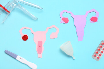 Paper uteruses with gynecological speculum, pills and pregnancy test on blue background
