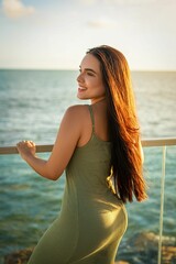 Young woman in a green dress enjoying a seaside view at sunset, with long hair