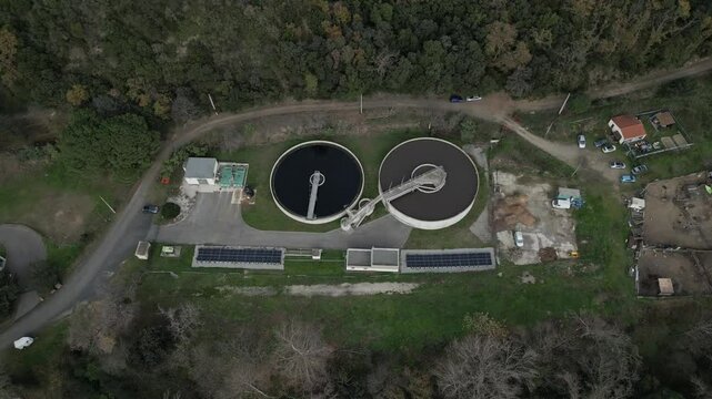 High angle view of a water treatment plant near amelie les bains, france, featuring circular filtration tanks, solar panels, and surrounding woodland