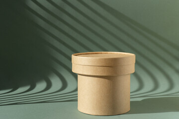 Brown cylindrical podium made of corrugated cardboard on green background with Light on wall. Concept mockup, copy space.