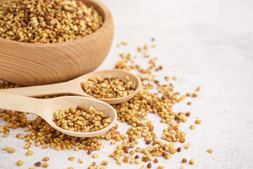 Wooden bowl and spoons with raw buckwheat grains on light background, closeup