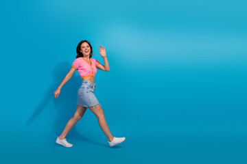 Young happy woman walking confidently in casual summer outfit against a bright blue background,...