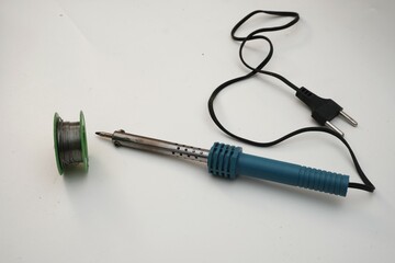 Soldering iron and a spool of green solder wire isolated on a white background, essential tools for electronics repairs and assembly.