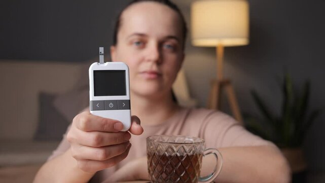 A young woman demonstrates how to use a glucometer to check her blood sugar levels while sitting at home. This simple activity is important for managing health and wellness