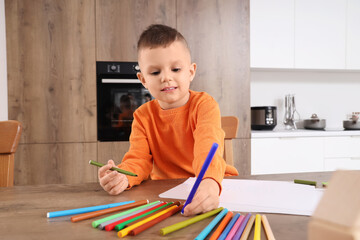 Cute little boy drawing with felt-tip pens on table in kitchen