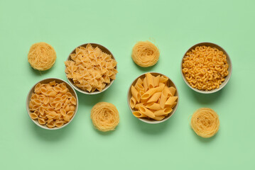 Bowls with different tasty uncooked pasta on green background