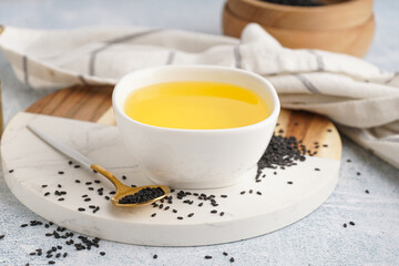 Bowl of oil with spoon and sesame seeds on white grunge background