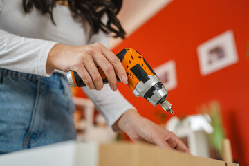 close up of woman hands use power drill to assemble furniture at home
