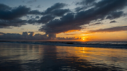 Obraz premium A serene sunset over the ocean, with the sun casting radiant orange and yellow hues across the sky