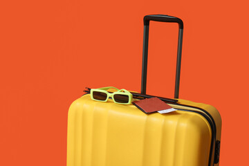 Yellow suitcase with passport and eyeglasses on orange background. Travel concept