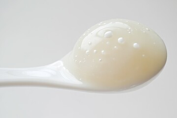 A dollop of creamy, off-white skincare product with air bubbles sits on a white spoon.