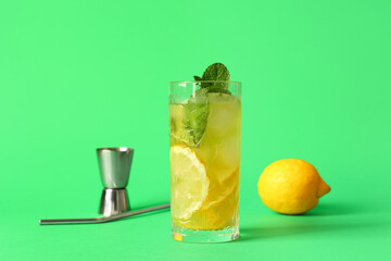 Glass of tasty lemonade with lemon, measuring cup and straw on green background
