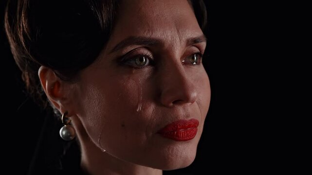 Retro woman actress with pin-up hairstyle and makeup isolated on black background crying in front of camera, tears flowing on cheek. Slow motion.