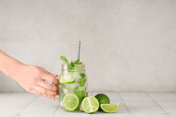 Female hand with mason jar of fresh Mojito cocktail on white background
