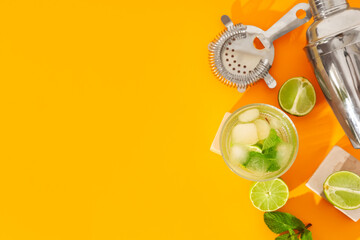 Glass of fresh mojito with cocktail strainer and shaker on orange background