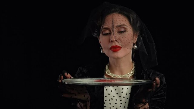 Retro woman actress with pin-up hairstyle and makeup isolated on black background, holding old vinyl record and blowing off white powder from surface. Slow motion.